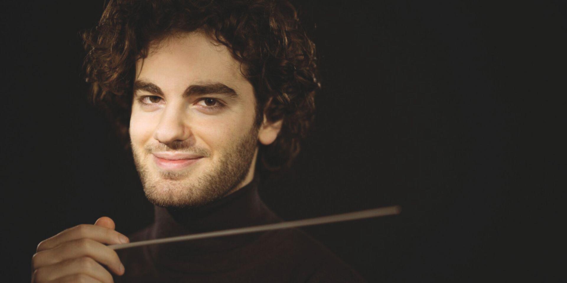 Ritratto in primo piano del direttore d'orchestra Emmanuel Tjeknavorian su sfondo nero.