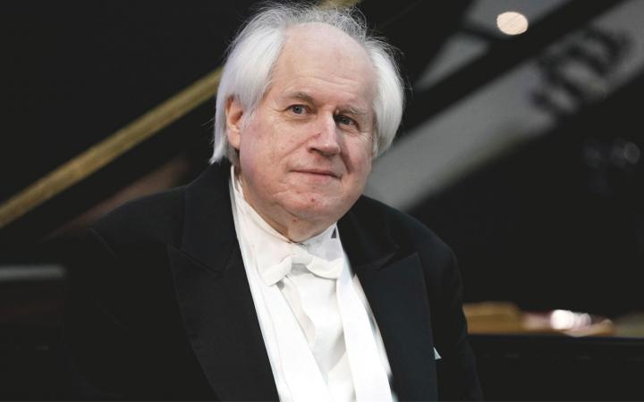 Ritratto a mezzo busto del pianista Grigory Sokolov con pianoforte alle spalle