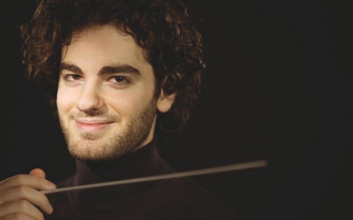 Ritratto in primo piano del direttore d'orchestra Emmanuel Tjeknavorian su sfondo nero.