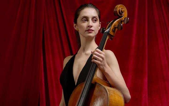 Una giovane donna con abito nero tiene in mano un violoncello con sguardo fiero 