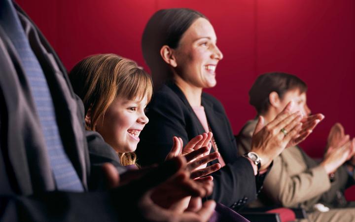 Una bambina sorride accanto alla mamma, applaudendo insieme agli altri