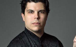 Andrea Battistoni vestito con una giacca nera damascata su fondo grigio